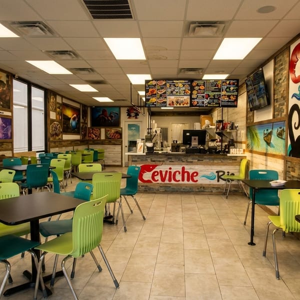 Interior of Ceviche Ria restaurant with empty tables, colorful chairs, and a counter with menus.