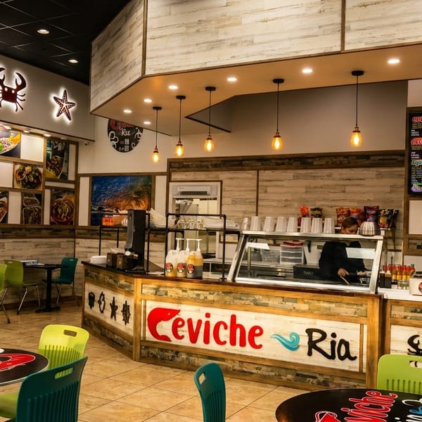 Interior of Ceviche Ria restaurant with tables, chairs, a counter, menu boards, and marine-themed decor.