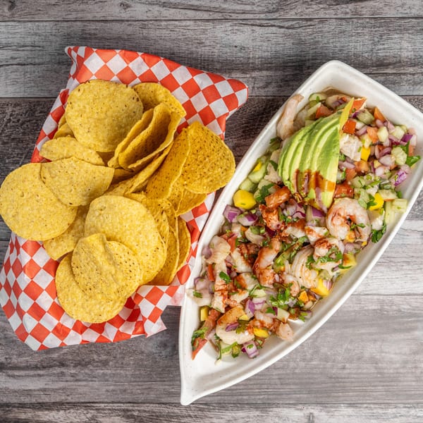Shrimp ceviche with avocado and salsa in a white dish, next to a basket of tortilla chips.
