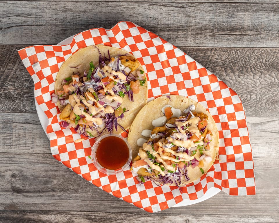 Two fish tacos with red cabbage, pico de gallo, and sauce, served with a side of salsa.