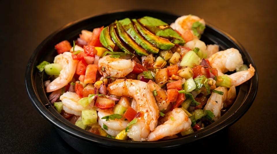 A vibrant shrimp ceviche bowl with avocado slices, tomatoes, cucumbers, and red onions.