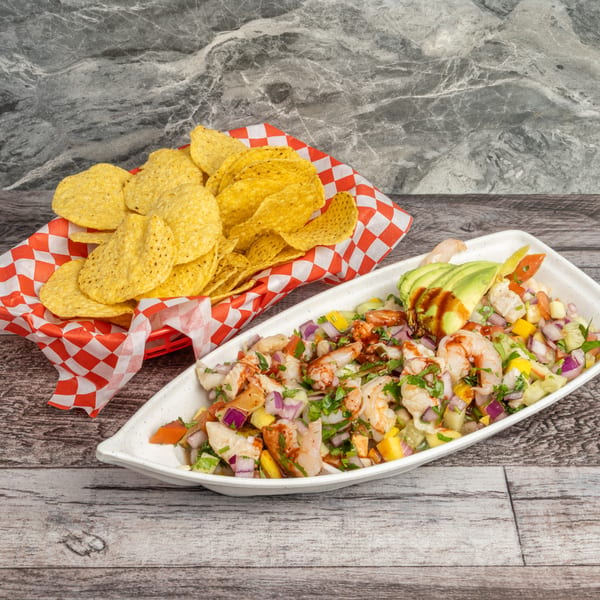 Shrimp ceviche with avocado and hot sauce, served with a basket of tortilla chips.