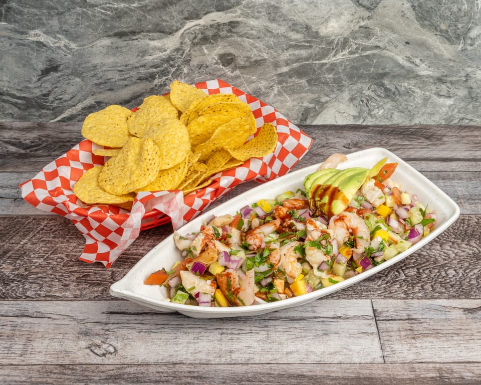 Shrimp ceviche with avocado and hot sauce, served with a basket of tortilla chips.
