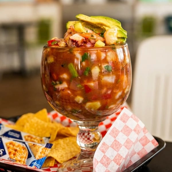 A large glass of ceviche topped with avocado, served with tortilla chips and crackers.