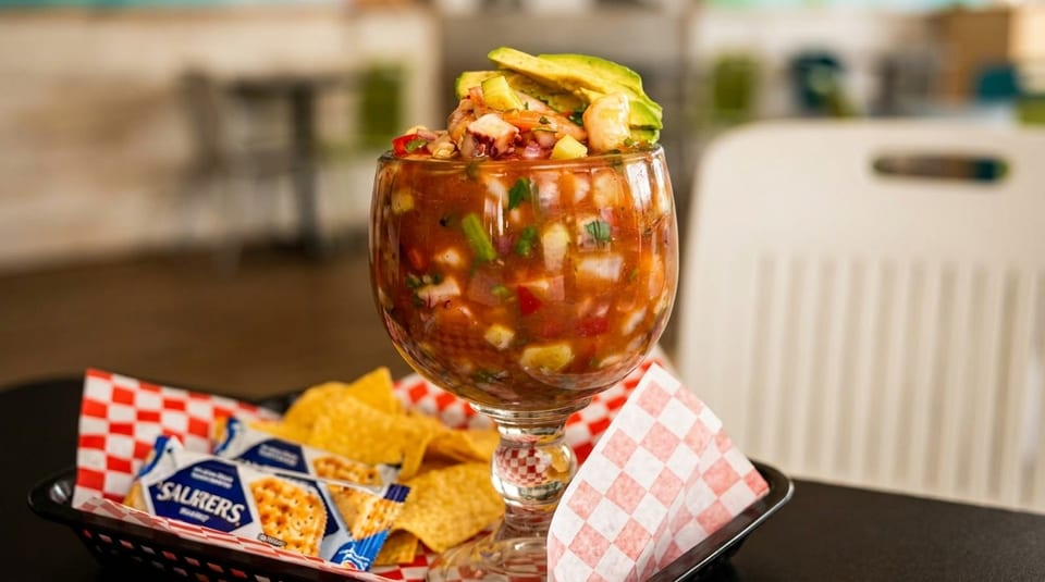 A large glass of ceviche topped with avocado, served with tortilla chips and crackers.