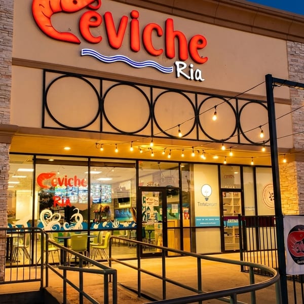 Exterior of Ceviche Ria restaurant at dusk, with a "WE ARE OPEN" banner and string lights.