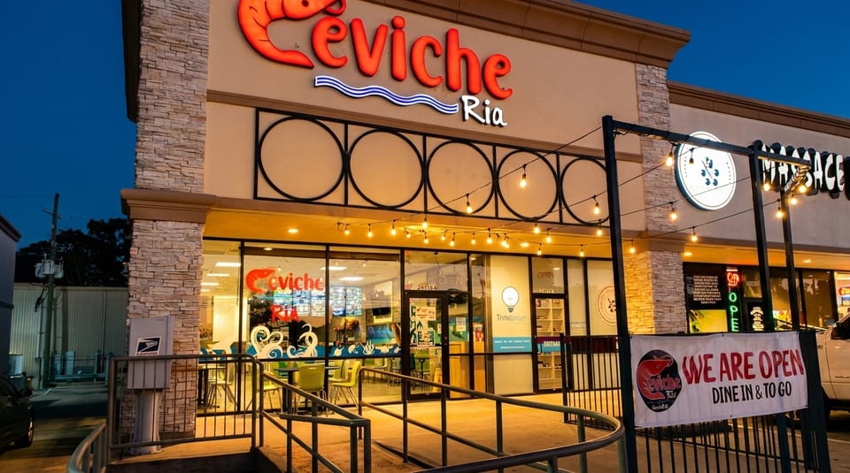 Exterior of Ceviche Ria restaurant at dusk, with a "WE ARE OPEN" banner and string lights.