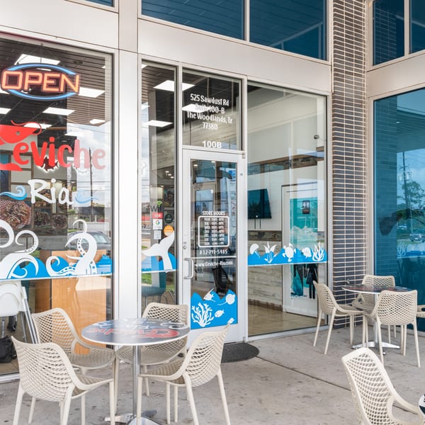 Exterior of Ceviche Ria restaurant with outdoor seating, an "OPEN" sign, and ocean-themed window decals.