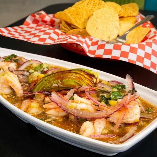 Shrimp ceviche with avocado, red onions, and cilantro, served with tortilla chips and orange juice.