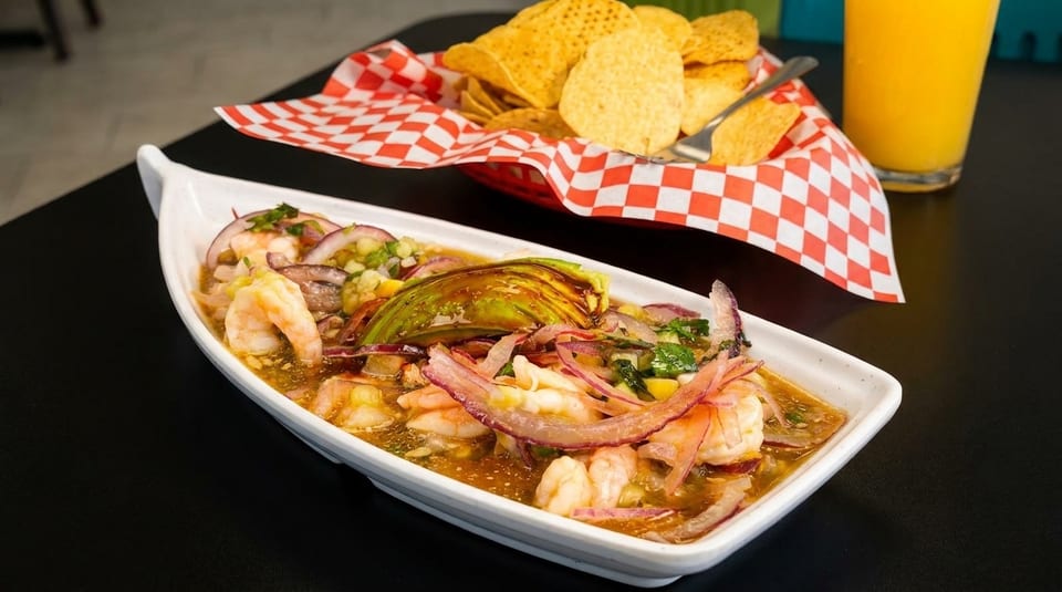 Shrimp ceviche with avocado, red onions, and cilantro, served with tortilla chips and orange juice.