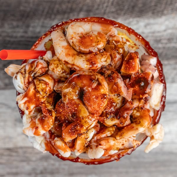Overhead view of a seafood cocktail with shrimp, octopus, and a red sauce, with a straw.