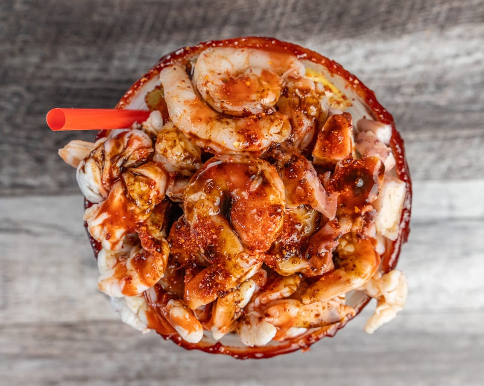 Overhead view of a seafood cocktail with shrimp, octopus, and a red sauce, with a straw.