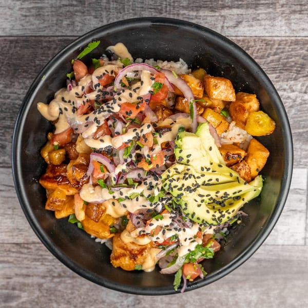 Overhead view of a poke bowl with chicken, avocado, red onion, tomatoes, and sesame seeds.