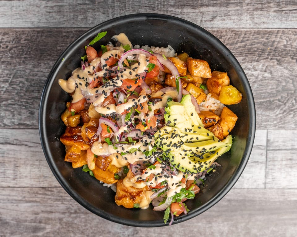 Overhead view of a poke bowl with chicken, avocado, red onion, tomatoes, and sesame seeds.